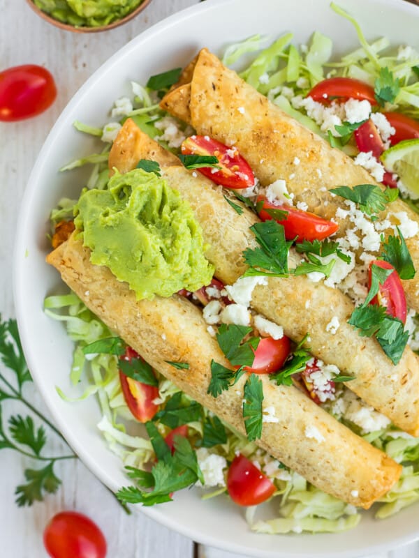 a plate of air fryer taquitos topped with cilantro, tomatoes, and guacamole