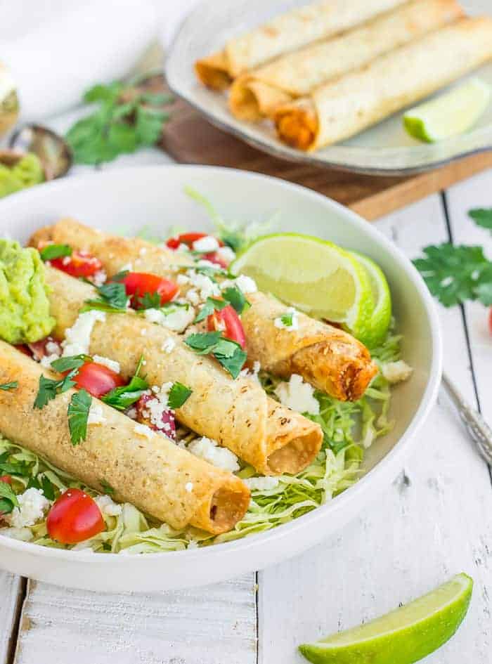 a plate of air fryer taquitos topped with cilantro, tomatoes, and guacamole