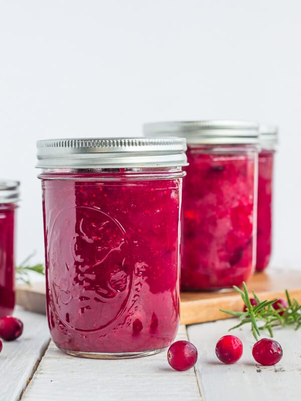 3 jars of homemade canned cranberry sauce with fresh cranberries on a white board