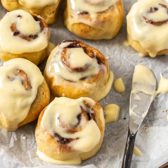 a knife with frosting and a tray of cinnamon rolls