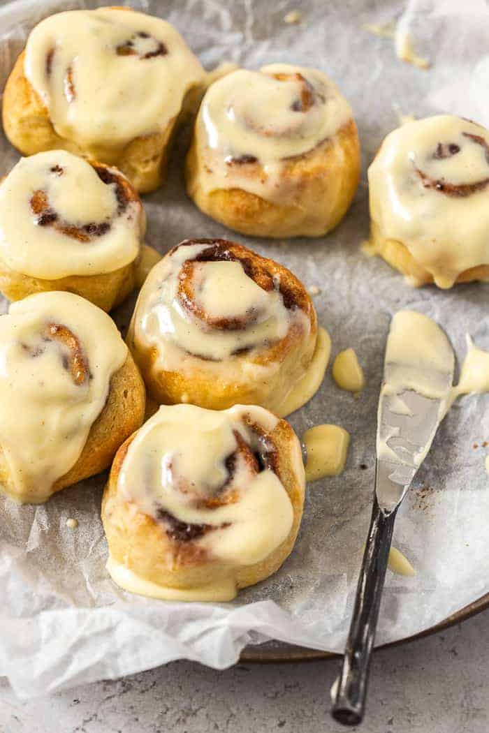 a knife with frosting and a tray of cinnamon rolls
