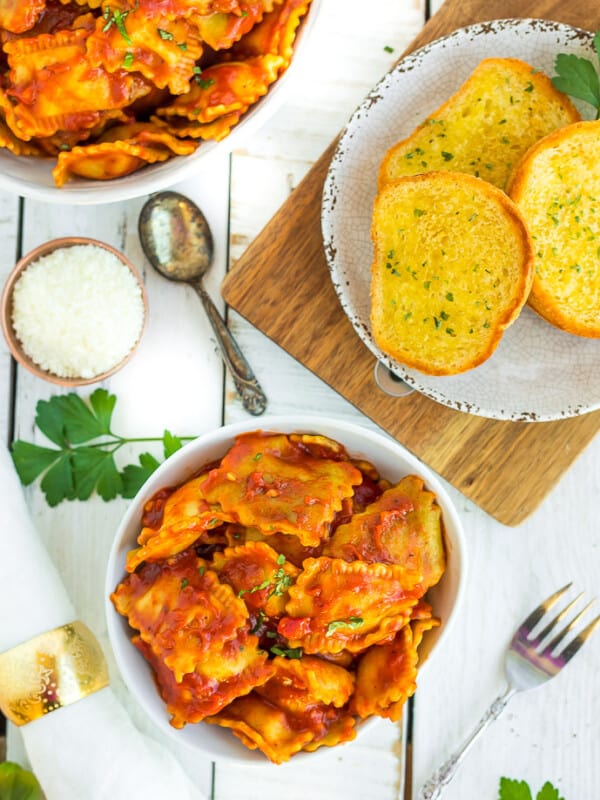 a white bowl of instant pot ravioli with garlic bread and fresh parsley