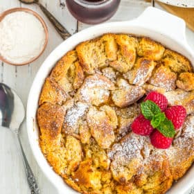 a white dish with eggnog bread pudding topped with raspberries