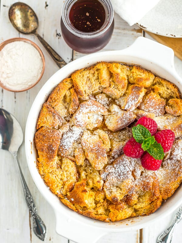 a white dish with eggnog bread pudding topped with raspberries