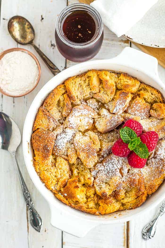 a white dish with eggnog bread pudding topped with raspberries