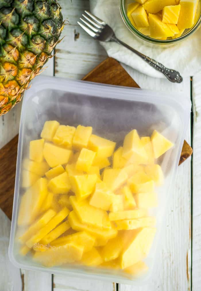 a silicone bag of pineapple slices on a wooden board with a whole pineapple and a small bowl of pineapple.