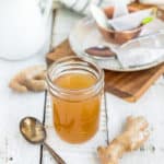 honey ginger syrup in a jar with a spoon and fresh ginger on a wooden board