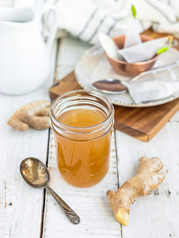 honey ginger syrup in a jar with a spoon and fresh ginger on a wooden board