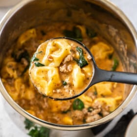 An Instant Pot full of Tortellini Soup with a ladle holding a scoop of the soup.
