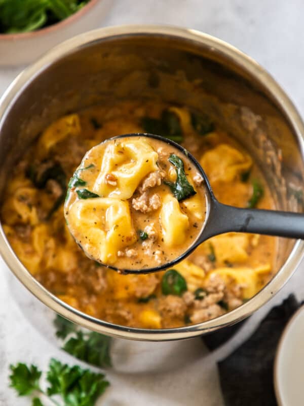 An Instant Pot full of Tortellini Soup with a ladle holding a scoop of the soup.