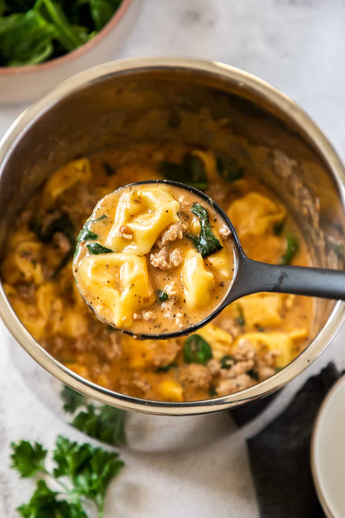 An Instant Pot full of Tortellini Soup with a ladle holding a scoop of the soup.