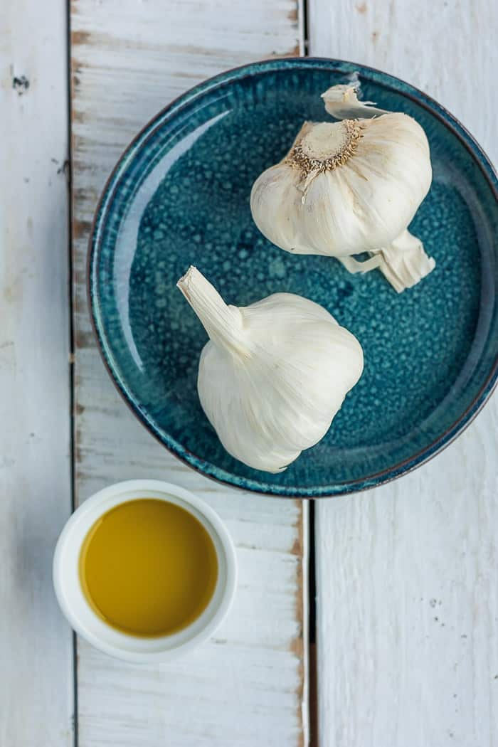 two heads of garlic on a blue plate with a small bowl of olive oil.