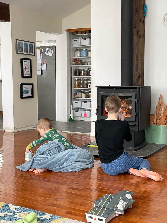 2 kids in front of a woodstove drinking cocoa