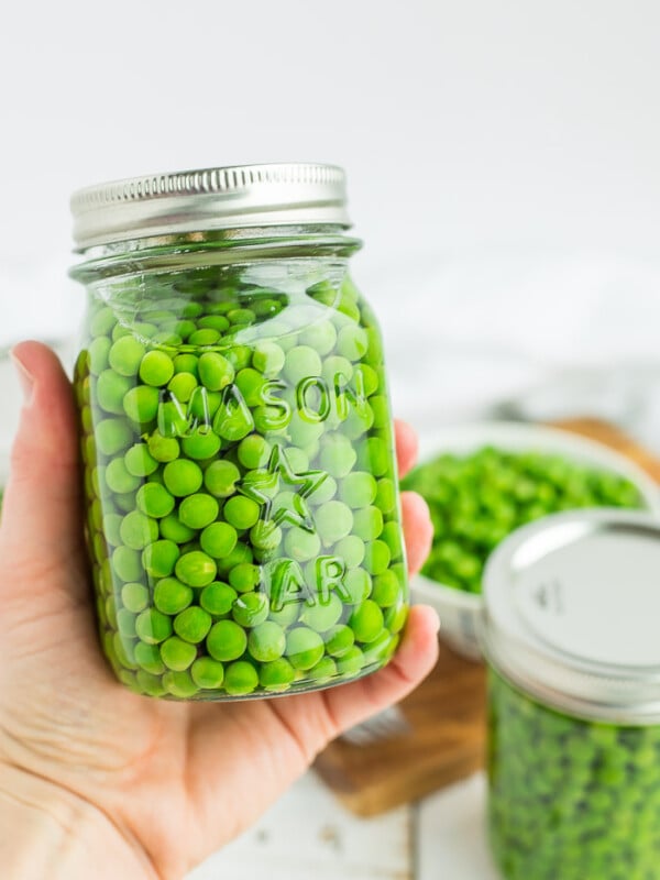 a hand holding a canning jar of peas