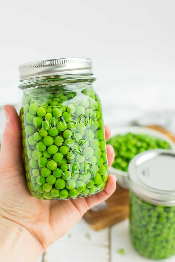a hand holding a canning jar of peas