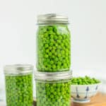 3 jars of green peas on a white board with a bowl of peas