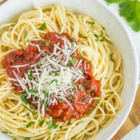 A white bowl of spaghetti topped with cheese and parsley