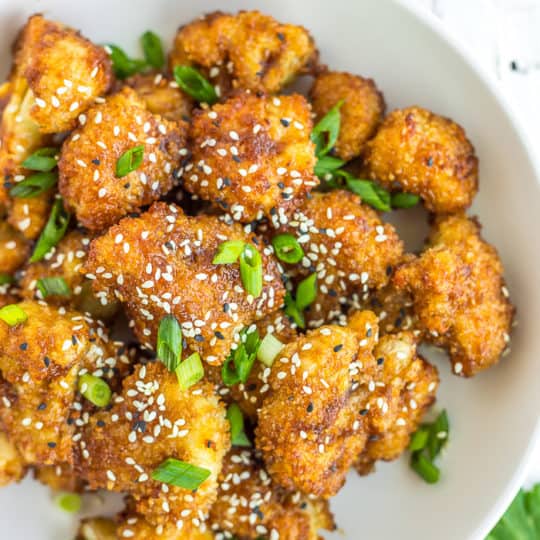 a white bowl of teriyaki cauliflower with black and white sesame seeds and sliced green onions