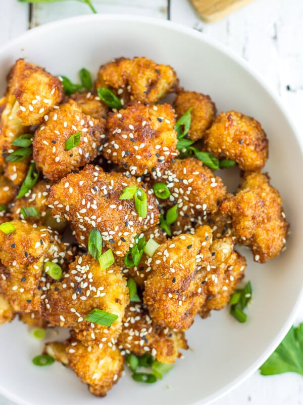 a white bowl of teriyaki cauliflower with black and white sesame seeds and sliced green onions