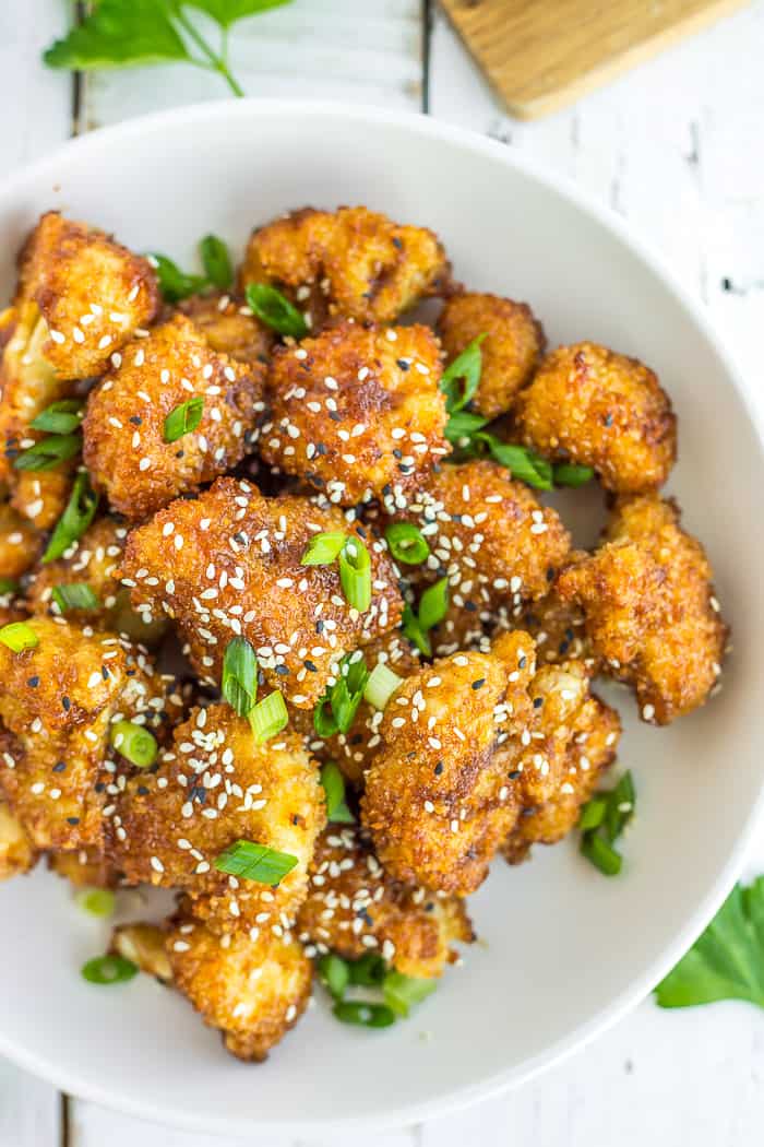 a white bowl of teriyaki cauliflower with black and white sesame seeds and sliced green onions