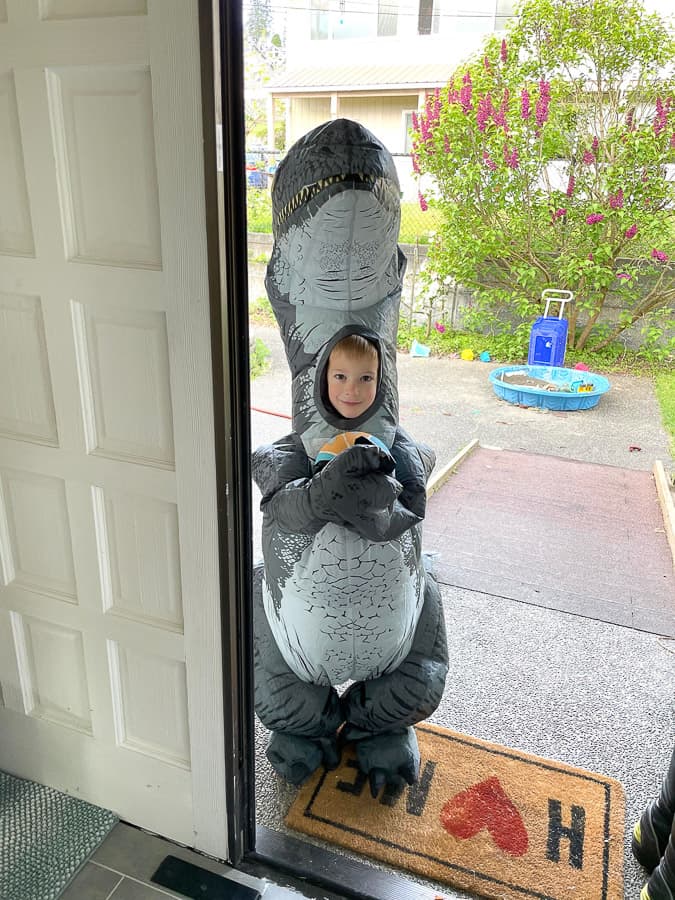 a boy in a dinosaur costume holding a basketball at a front door