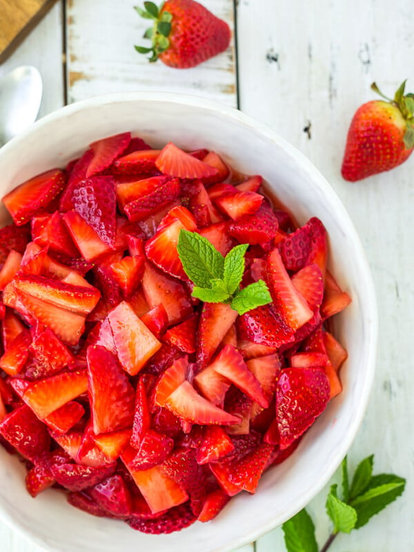 A bowl of sugared straweberries topped with mint on a white board