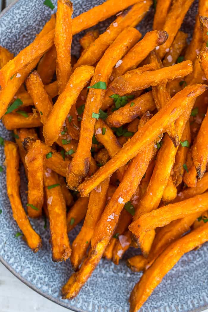 sweet potato fries on a plate topped with salt and chopped parsley