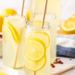 multiple glasses of rose lemonade with slices of lemon and rose petals on a white board