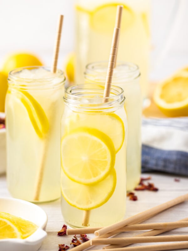 multiple glasses of rose lemonade with slices of lemon and rose petals on a white board