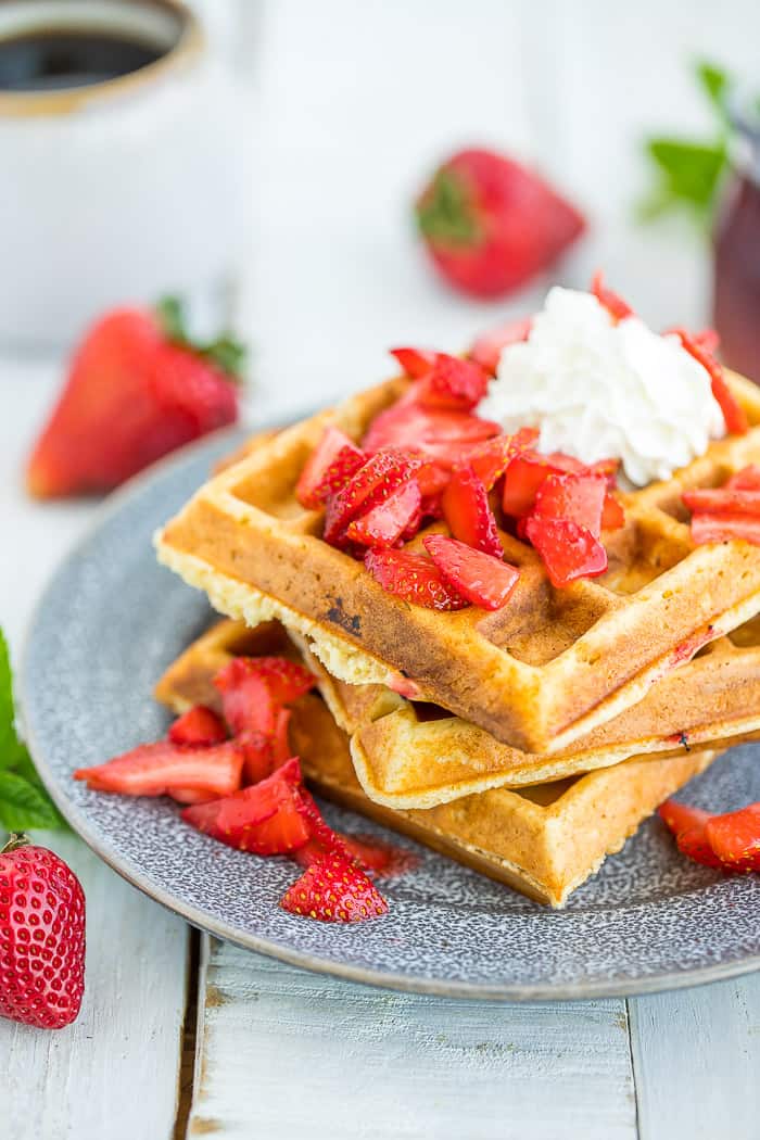 Strawberry waffles topped with sliced strawberries and whipped cream