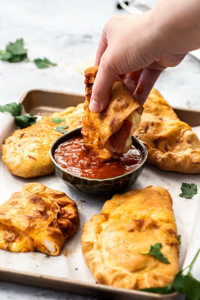 A handing dipping a calzone into a dish of pizza sauce