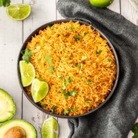 a black bowl of Instant Pot Mexican rice topped with cilantro and lime wedges.