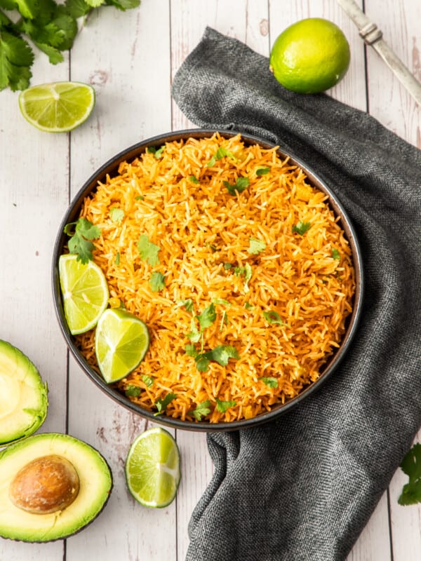 a black bowl of Instant Pot Mexican rice topped with cilantro and lime wedges.