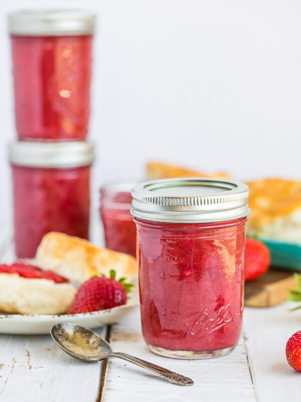 Multiple jars of strawberry rhubarb jam on a white board and a biscuit