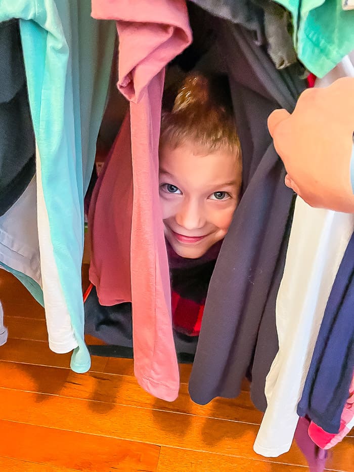 a boy hiding in clothes in a closet