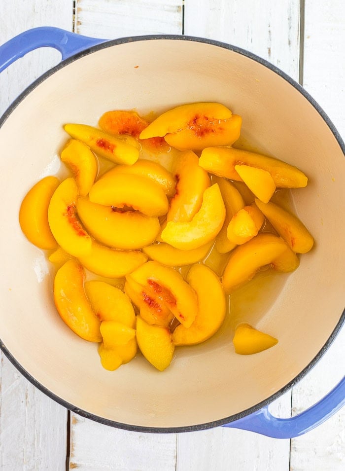 a blue dutch oven full of sliced peaches.