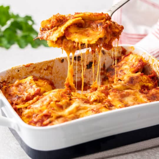 a spatula scooping ravioli lasagna out of a baking dish with cheese stretching