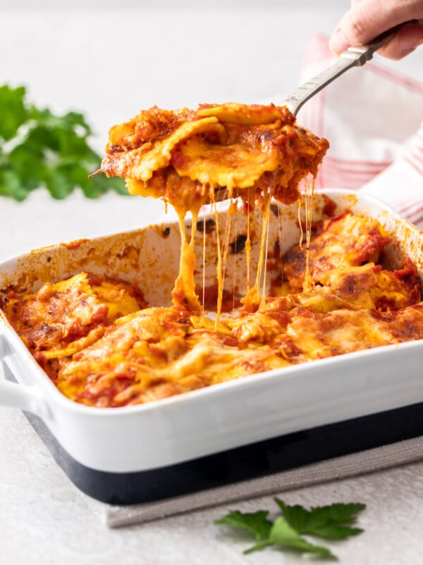 a spatula scooping ravioli lasagna out of a baking dish with cheese stretching
