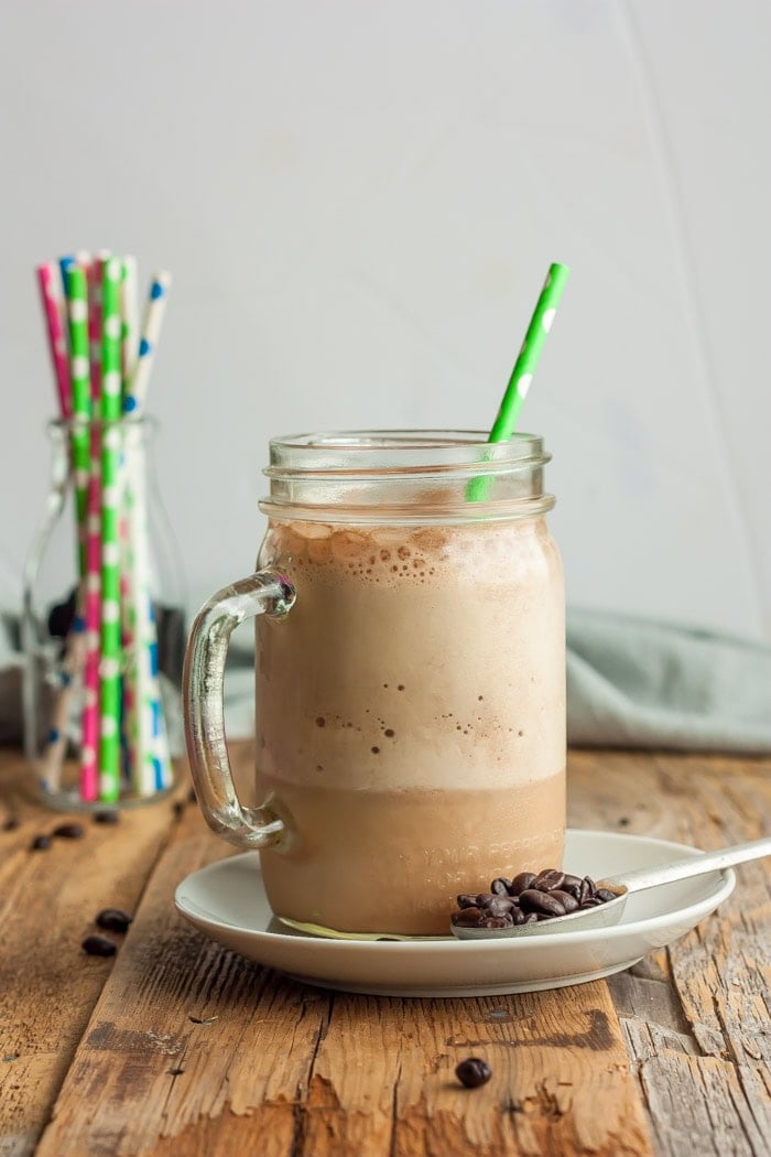 a glass jar of blended iced coffee with a green polka-dot straw in it.
