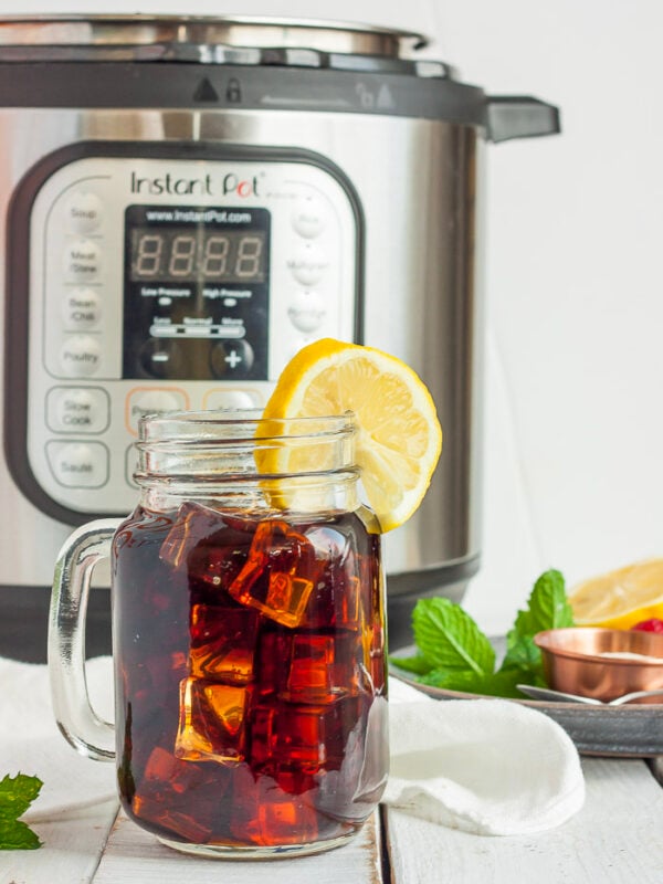 a canning jar full of Instant Pot iced team with a slice of lemon in front of an Instant Pot.