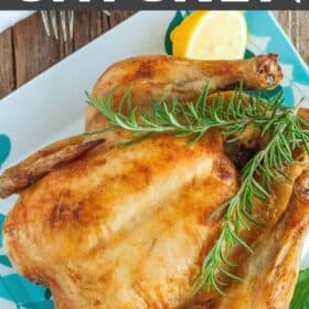 a whole roasted chicken on a plate with rosemary and sliced lemons