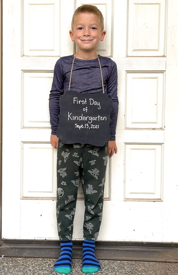 a boy holding a sign that says "first day of kindergarten" in front of a white door