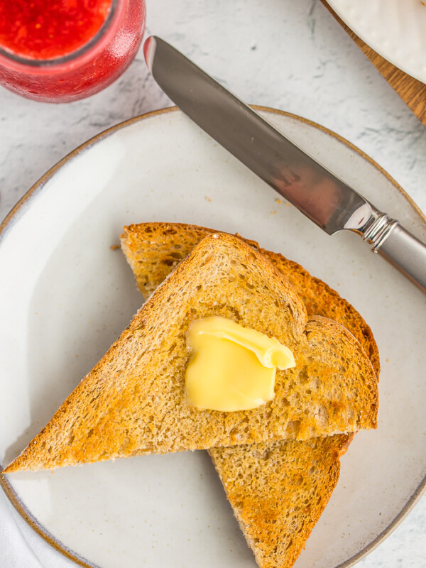 air fried toast with a pat of butter on a plate with a knife and strawberry jam