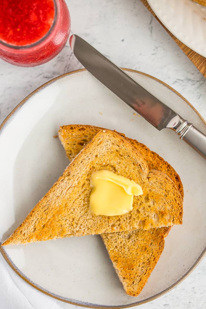 air fried toast with a pat of butter on a plate with a knife and strawberry jam