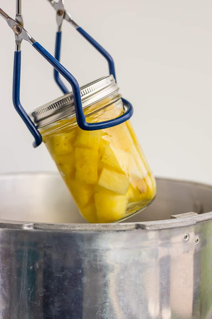 Canning tongs lifting a mason jar of cubed pineapple out of a canner