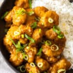 a bowl of air fryer orange chicken topped with green onions in a bowl with white rice and orange slices