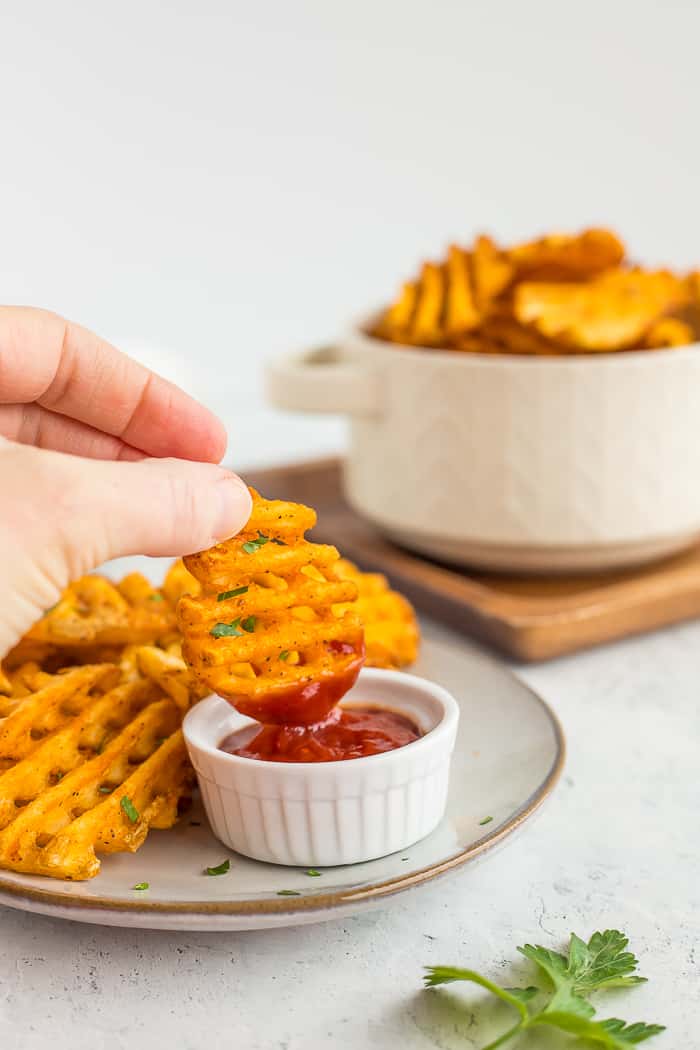 a hand dipping a waffle fry into a dish of ketchup