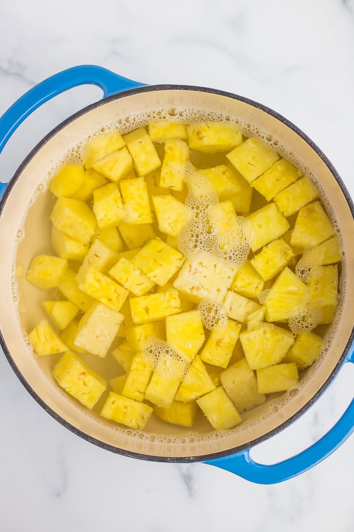 a blue dutch oven with water and pineapple cubes.