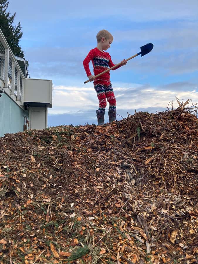 a boy with a shovel standing on top of a pile of woodchips