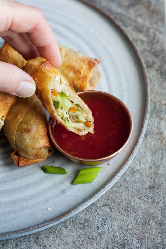 a hand dipping an egg roll into a sauce.